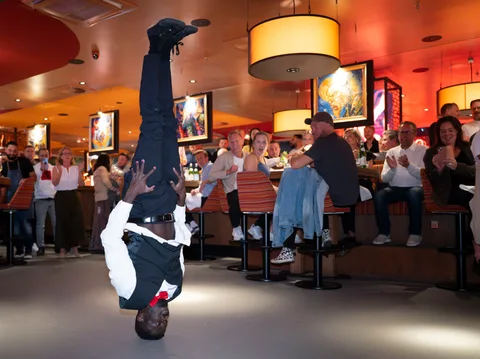 Ein Showkellner im Kopfstand vor staunenden und applaudierenden Gästen im Restaurant.