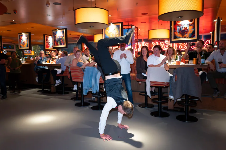 Ein Showkellner zeigt einen Handstand vor lachenden und applaudierenden Gästen.