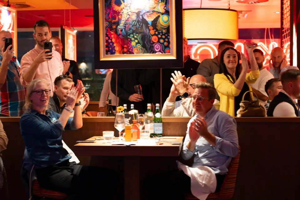 Gäste applaudieren an den Restauranttischen und halten den Showmoment mit dem Handy fest.