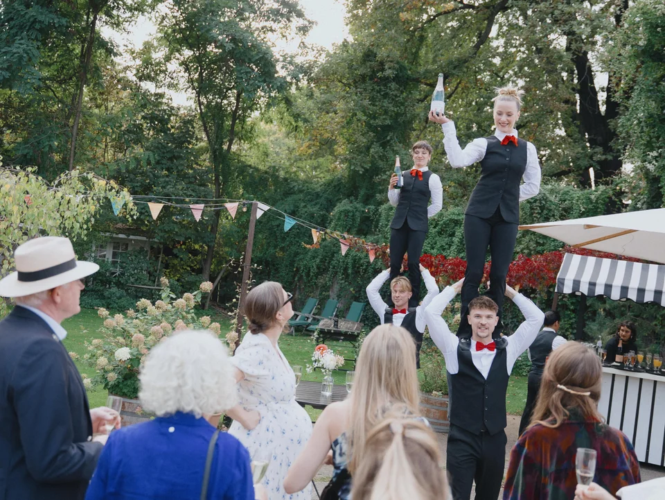 Zwei Showkellnerinnen stehen auf den Schultern ihrer Kollegen zwischen den Hochzeitsgästen im Garten.