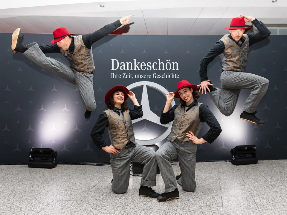 Vier Künstler von The Funky Monkeys mit roten Hüten vor einer Mercedes-Benz-Fotowand.